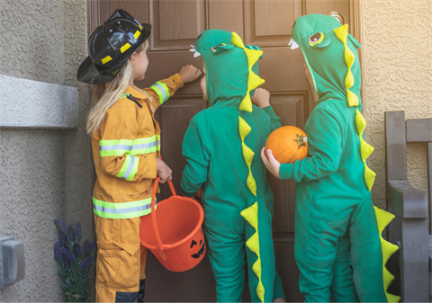 Children trick or treating in firefighter and dinosaur costumes