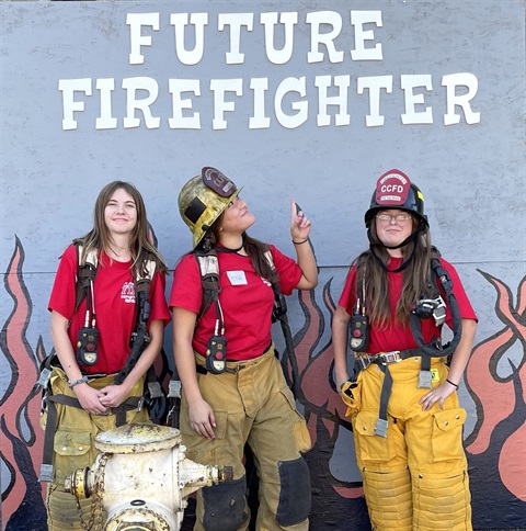 Three Girls Standing Under Future Firefighter Sign